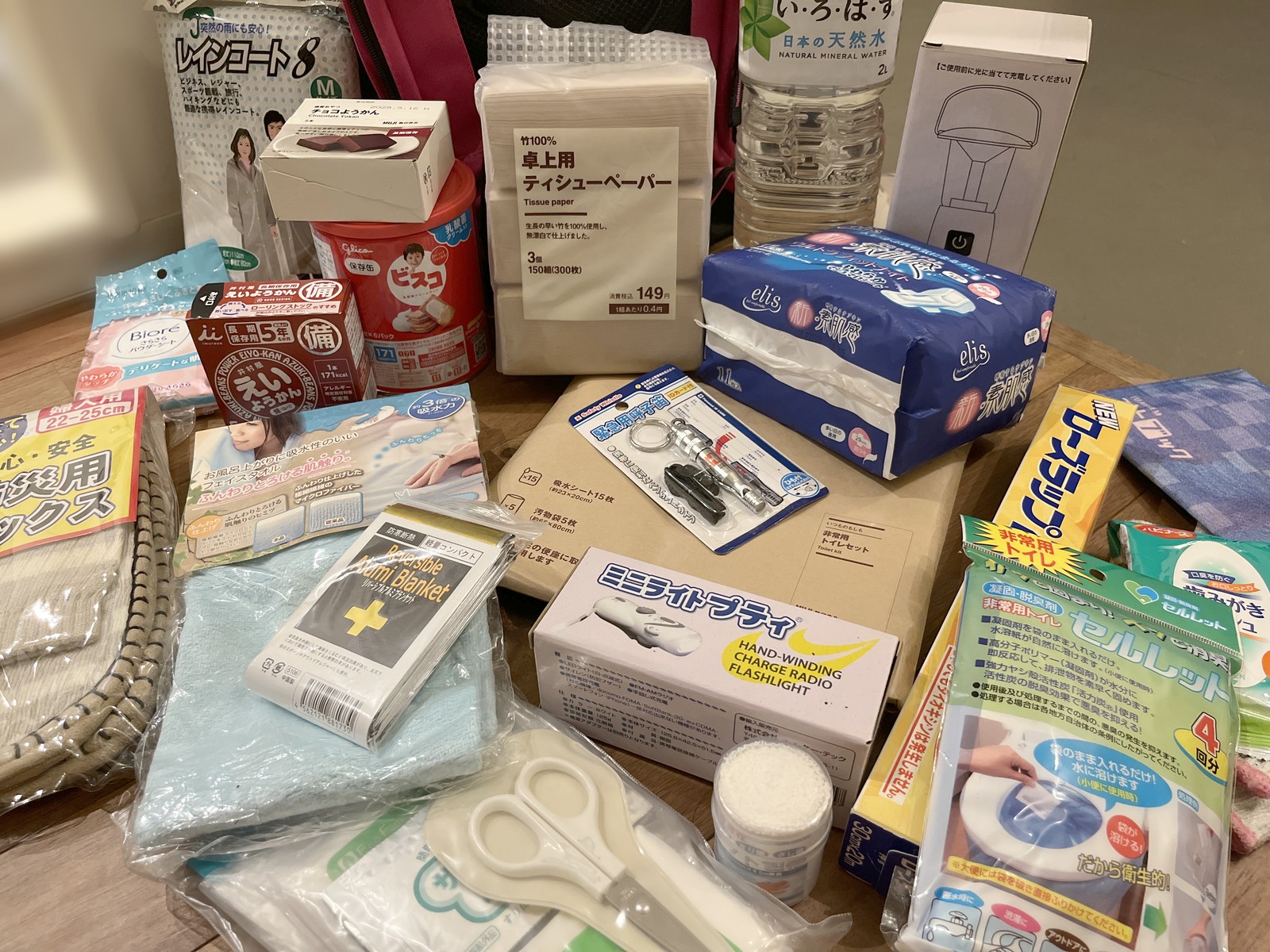 防災リュックから出した中身を床に並べた写真。携帯トイレ2種類、手回し充電のラジオライト、緊急用呼子笛、アルミブランケット、保存食、ティッシュなどが見える