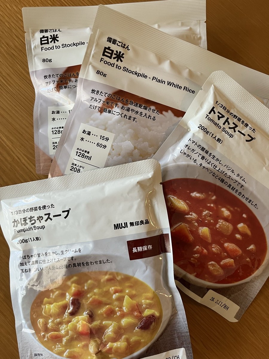 買い足した無印良品の長期保存食。かぼちゃスープとトマトスープの袋、備蓄ごはん白米の袋が木のテーブルに並んでいる