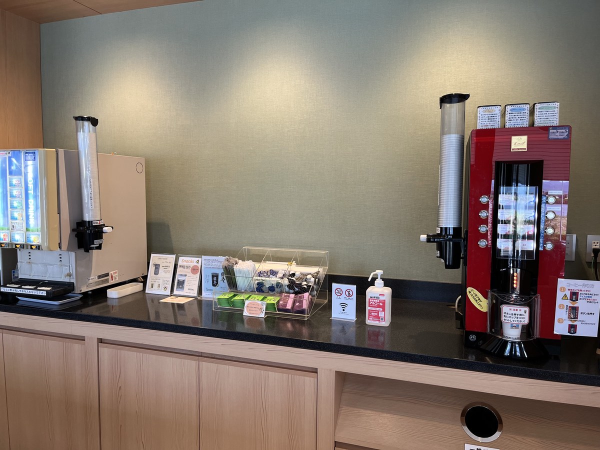 ラウンジのドリンクコーナー。ソフトドリンクのサーバーとコーヒーマシン、有料のおつまみの案内が並んでいる