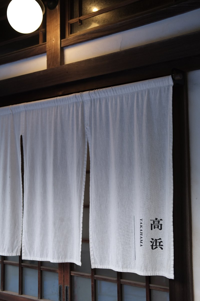 部屋の入口にかかる白い暖簾。高浜 TAKAHAMAと書かれている